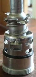 The spear once lifted out: spring and clip at the top, the slotted cage in the middle, the black seal and threaded base below.
